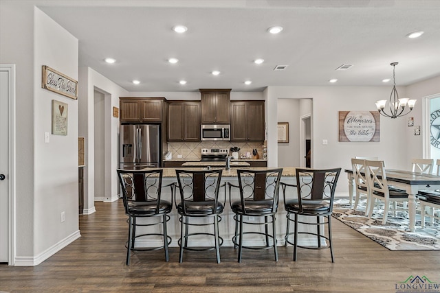 kitchen featuring a center island with sink, decorative backsplash, stainless steel appliances, dark hardwood / wood-style flooring, and a chandelier