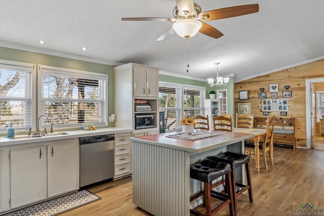 kitchen with white cabinetry, wood walls, a kitchen island, stainless steel dishwasher, and sink