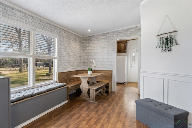 dining space with a textured ceiling, a healthy amount of sunlight, brick wall, and vaulted ceiling