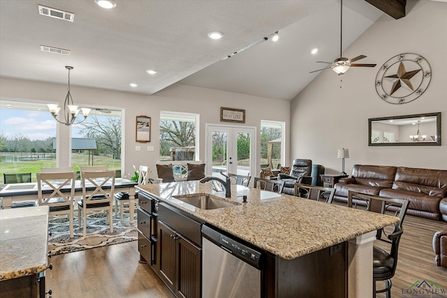 kitchen with light stone countertops, dark brown cabinetry, sink, a kitchen island with sink, and stainless steel dishwasher