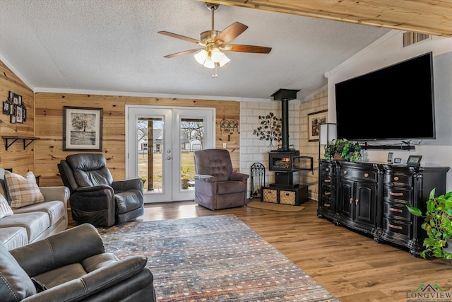 living room with vaulted ceiling, wooden walls, a wood stove, a textured ceiling, and french doors