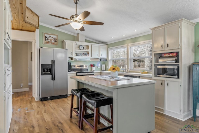 kitchen featuring lofted ceiling, a center island, a kitchen bar, appliances with stainless steel finishes, and a textured ceiling