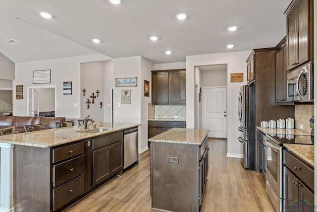 kitchen featuring stainless steel appliances, tasteful backsplash, sink, light stone counters, and a center island with sink