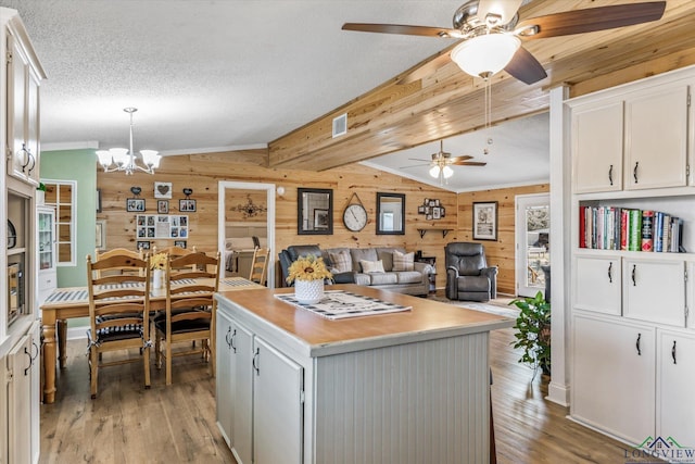 kitchen with hanging light fixtures, white cabinets, a center island, and wood walls