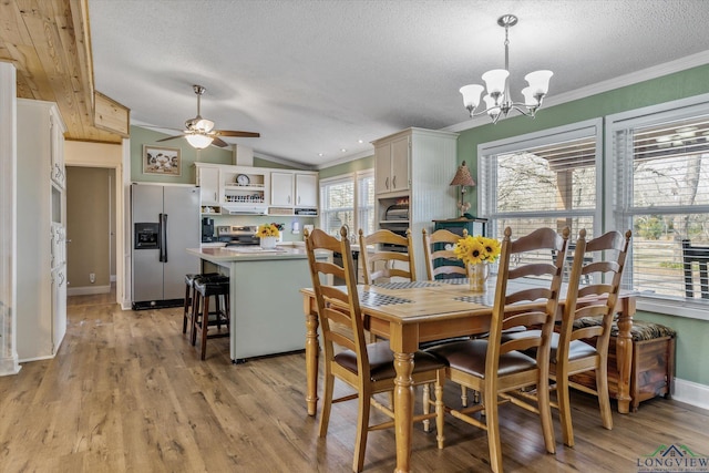 dining space with ceiling fan with notable chandelier, light hardwood / wood-style flooring, ornamental molding, and vaulted ceiling