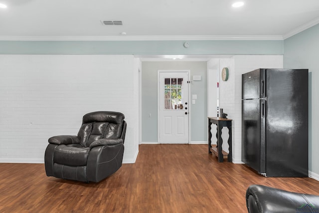 living area featuring wood finished floors, ornamental molding, baseboards, brick wall, and recessed lighting