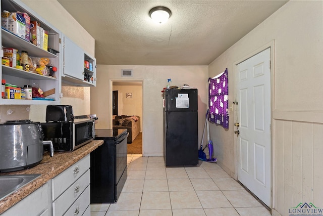 kitchen featuring sink, a textured ceiling, light tile patterned floors, black refrigerator, and white cabinets