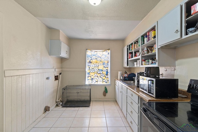 kitchen featuring sink, wood walls, black electric range, a textured ceiling, and light tile patterned floors