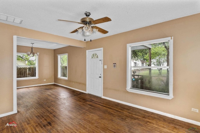 foyer with a textured ceiling, ceiling fan with notable chandelier, a healthy amount of sunlight, and dark wood-type flooring