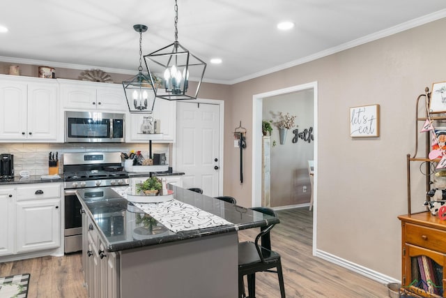 kitchen with a kitchen island, appliances with stainless steel finishes, decorative light fixtures, white cabinets, and crown molding