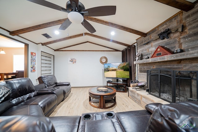 living room with wood walls, a stone fireplace, light hardwood / wood-style flooring, vaulted ceiling with beams, and ceiling fan