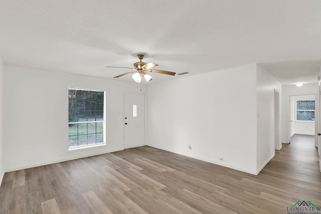 empty room featuring ceiling fan, a healthy amount of sunlight, and light hardwood / wood-style floors