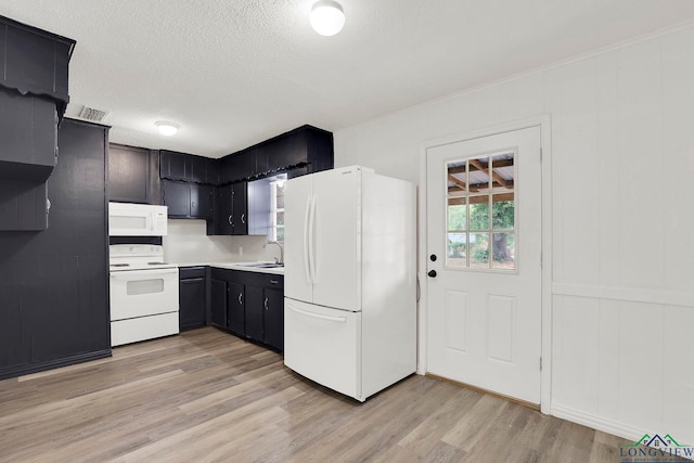 kitchen with a textured ceiling, light wood-type flooring, white appliances, and sink