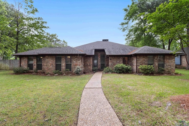 view of front of property with fence, roof with shingles, a front yard, and brick siding