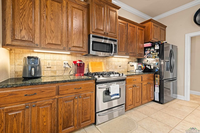 kitchen with light tile patterned floors, stainless steel appliances, ornamental molding, and dark stone countertops