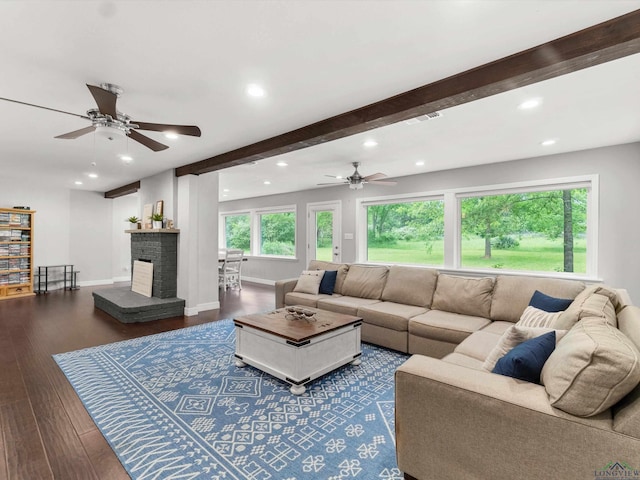 living room featuring beamed ceiling, a brick fireplace, ceiling fan, and dark wood-type flooring