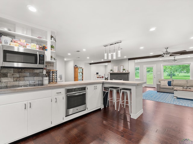 kitchen with kitchen peninsula, appliances with stainless steel finishes, tasteful backsplash, white cabinetry, and hanging light fixtures