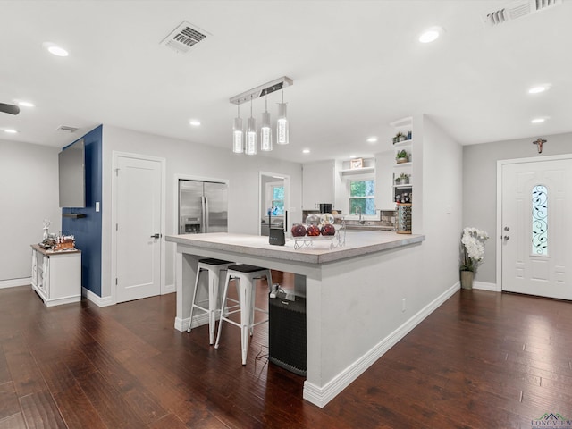 kitchen featuring white cabinetry, stainless steel refrigerator with ice dispenser, kitchen peninsula, pendant lighting, and a kitchen bar