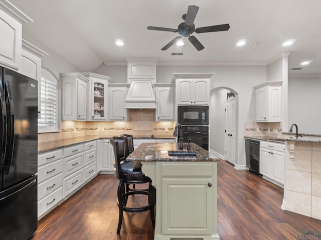 kitchen with white cabinets, dark hardwood / wood-style flooring, a kitchen bar, black appliances, and a center island with sink