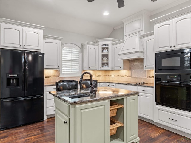 kitchen with white cabinets, dark stone counters, a kitchen island with sink, and black appliances