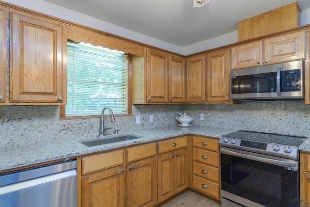 kitchen with appliances with stainless steel finishes, sink, light stone countertops, and tasteful backsplash