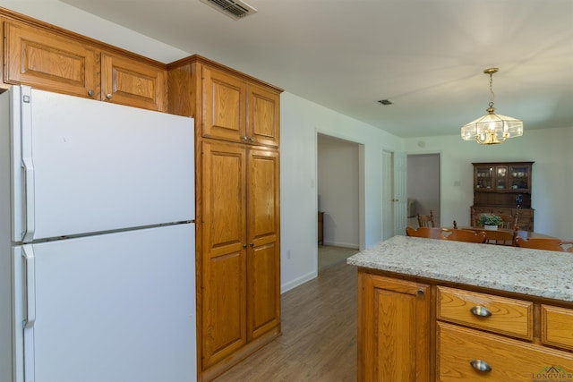 kitchen featuring light wood-type flooring, light stone counters, a notable chandelier, white fridge, and hanging light fixtures