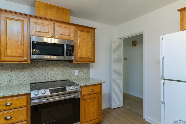 kitchen with wood-type flooring, light stone countertops, appliances with stainless steel finishes, and tasteful backsplash