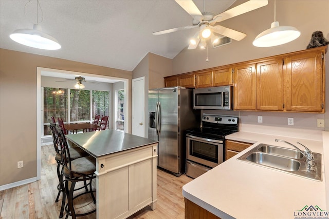 kitchen with a kitchen breakfast bar, stainless steel appliances, vaulted ceiling, sink, and pendant lighting