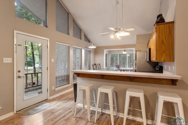 kitchen featuring stainless steel fridge, a kitchen breakfast bar, light hardwood / wood-style floors, and kitchen peninsula