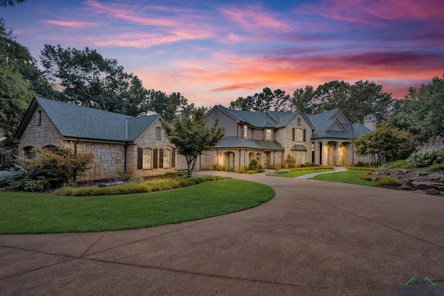 french provincial home with stone siding, concrete driveway, and a lawn