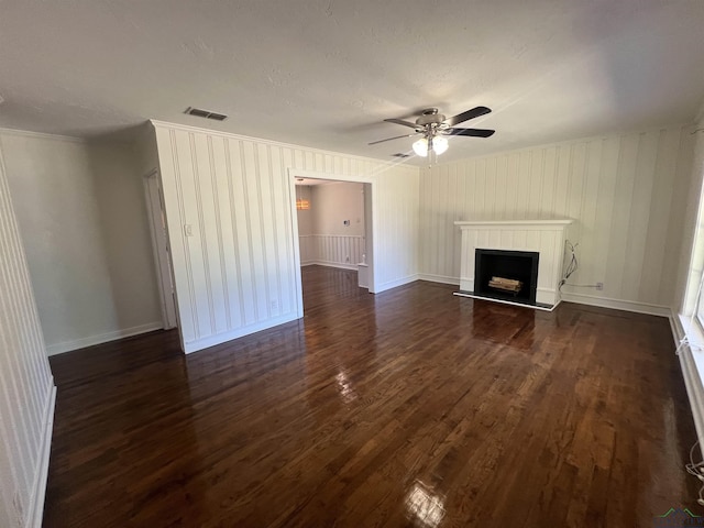 unfurnished living room with a fireplace with raised hearth, dark wood-style floors, visible vents, a ceiling fan, and crown molding