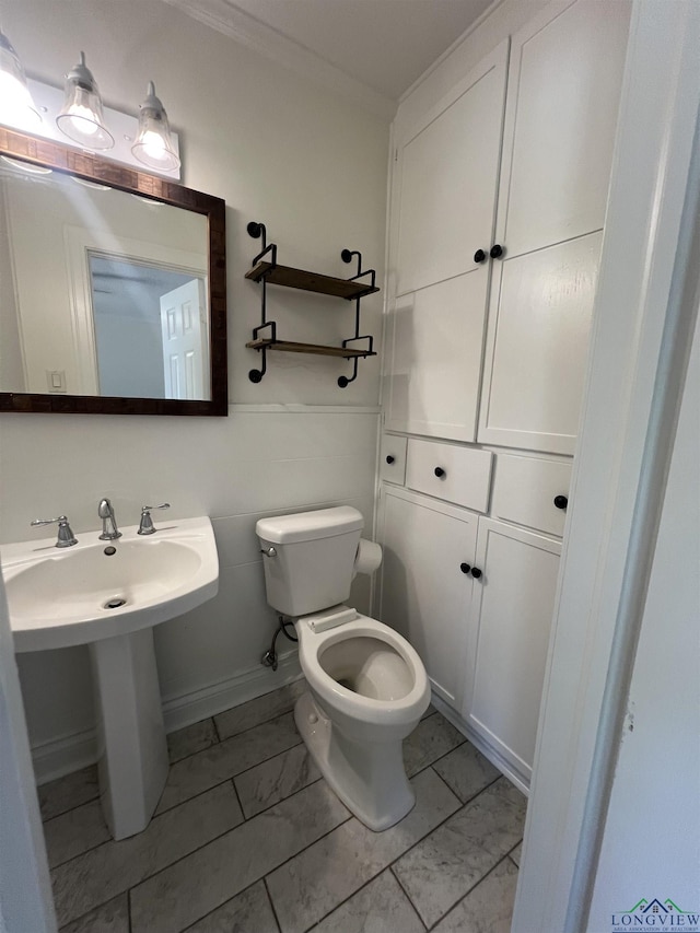 bathroom with toilet, marble finish floor, and crown molding