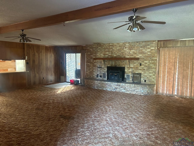 unfurnished living room with ceiling fan, beamed ceiling, wood walls, a textured ceiling, and carpet