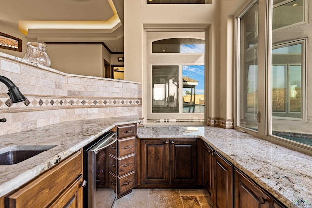 kitchen with sink, tasteful backsplash, light stone counters, stainless steel dishwasher, and a tray ceiling