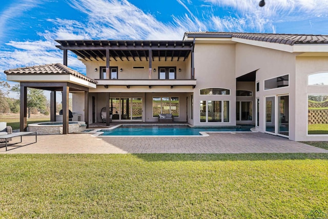 rear view of property with a lawn, a swimming pool with hot tub, a balcony, and a patio