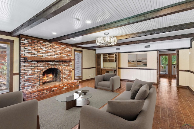 living room featuring hardwood / wood-style floors, a fireplace, beamed ceiling, and an inviting chandelier