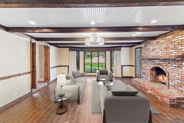 living room featuring beam ceiling, an inviting chandelier, and a brick fireplace