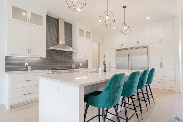 kitchen with white cabinetry, a kitchen island with sink, and wall chimney exhaust hood