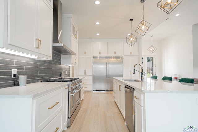 kitchen with premium appliances, wall chimney range hood, sink, pendant lighting, and white cabinets