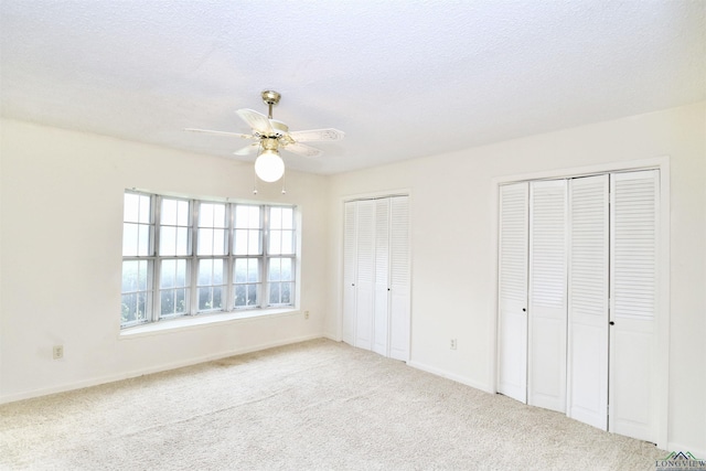 unfurnished bedroom featuring carpet flooring, ceiling fan, a textured ceiling, and two closets