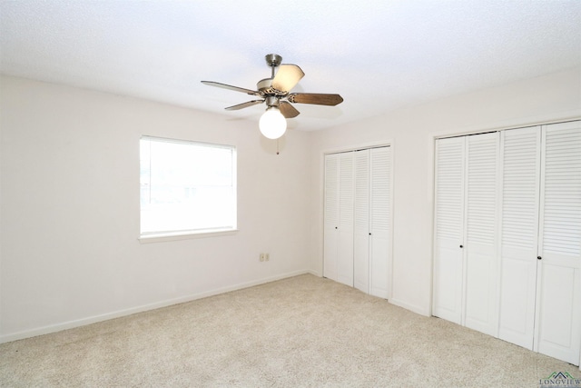 unfurnished bedroom featuring multiple closets, ceiling fan, and light colored carpet