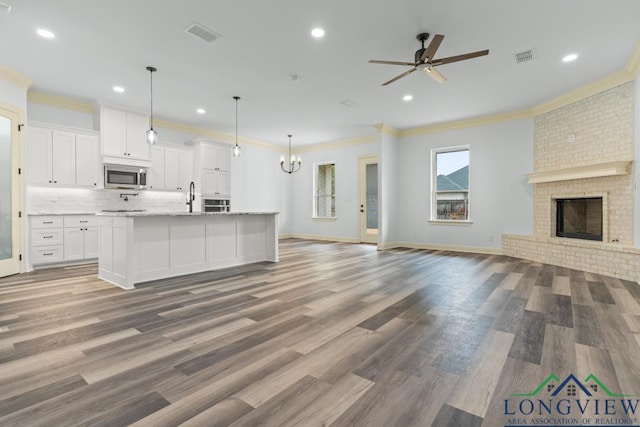 kitchen featuring a fireplace, white cabinets, hanging light fixtures, and ceiling fan with notable chandelier