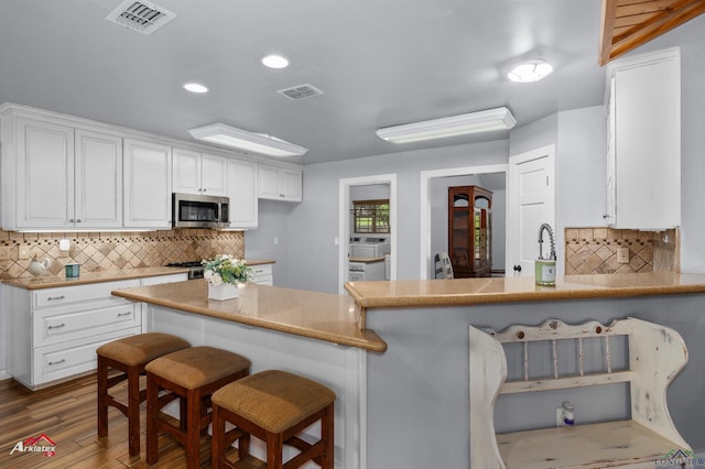 3718 Ben Hogan Dr, Longview, TX 75605 - kitchen with stainless steel microwave, a breakfast bar, backsplash, white cabinetry, and recessed lighting