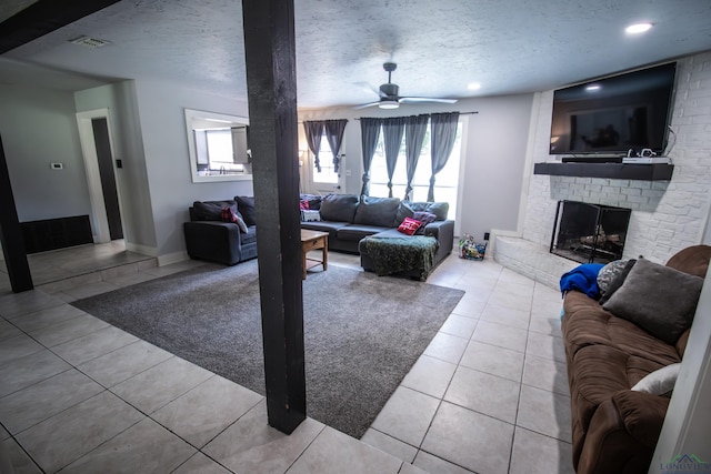 living room with ceiling fan, a fireplace, light tile patterned floors, and a textured ceiling