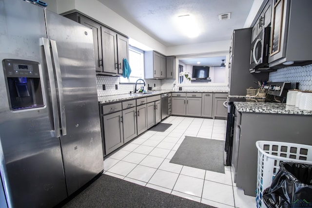 kitchen featuring gray cabinetry, stainless steel appliances, sink, light tile patterned floors, and stone countertops