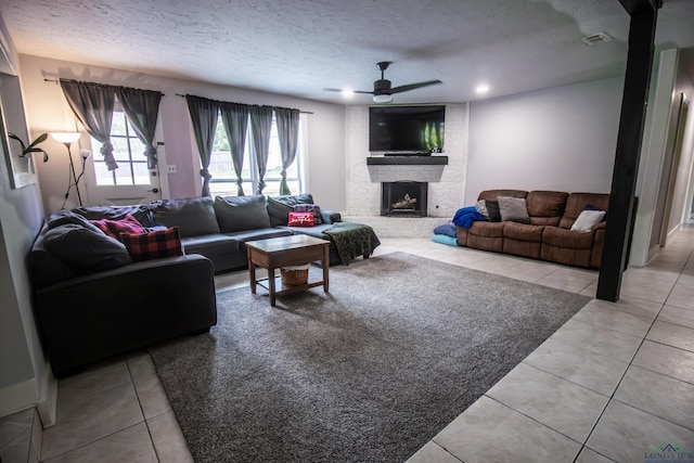 living room with a fireplace, a textured ceiling, ceiling fan, and light tile patterned flooring