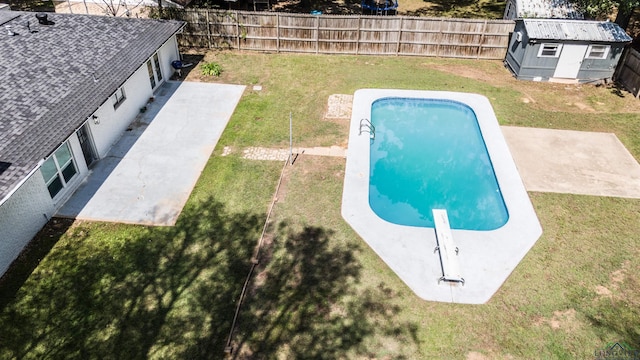 view of swimming pool with a yard, a diving board, a patio, and a storage unit