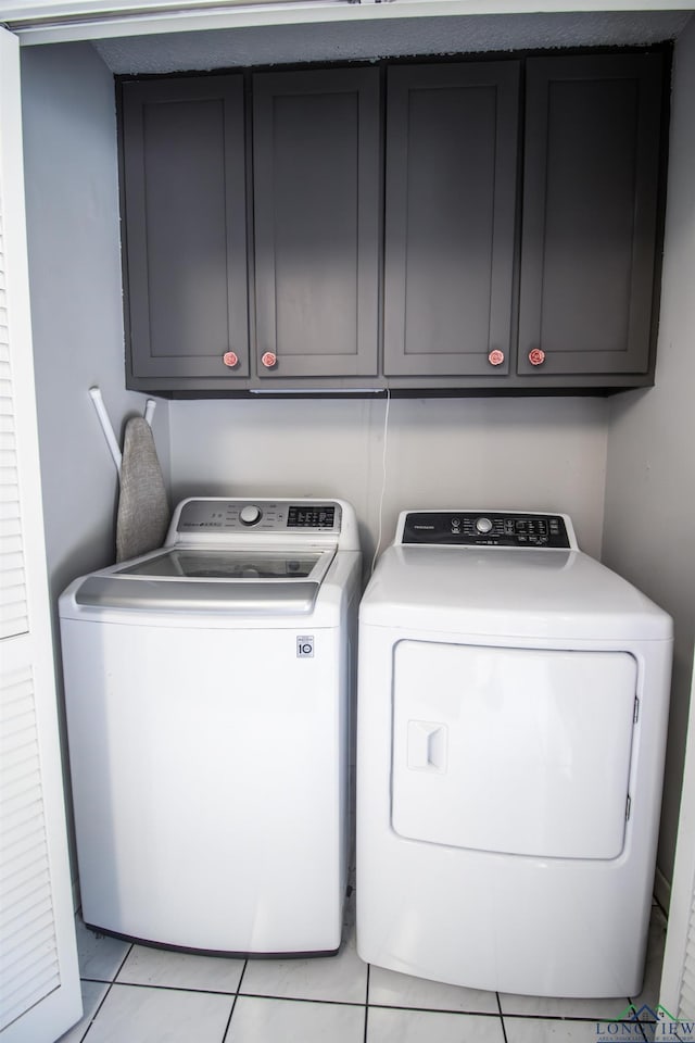 laundry area featuring separate washer and dryer, light tile patterned floors, and cabinets