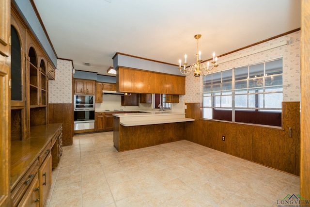 kitchen with kitchen peninsula, built in microwave, crown molding, a chandelier, and hanging light fixtures