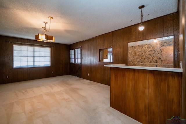 interior space with carpet, a textured ceiling, wooden walls, pendant lighting, and an inviting chandelier